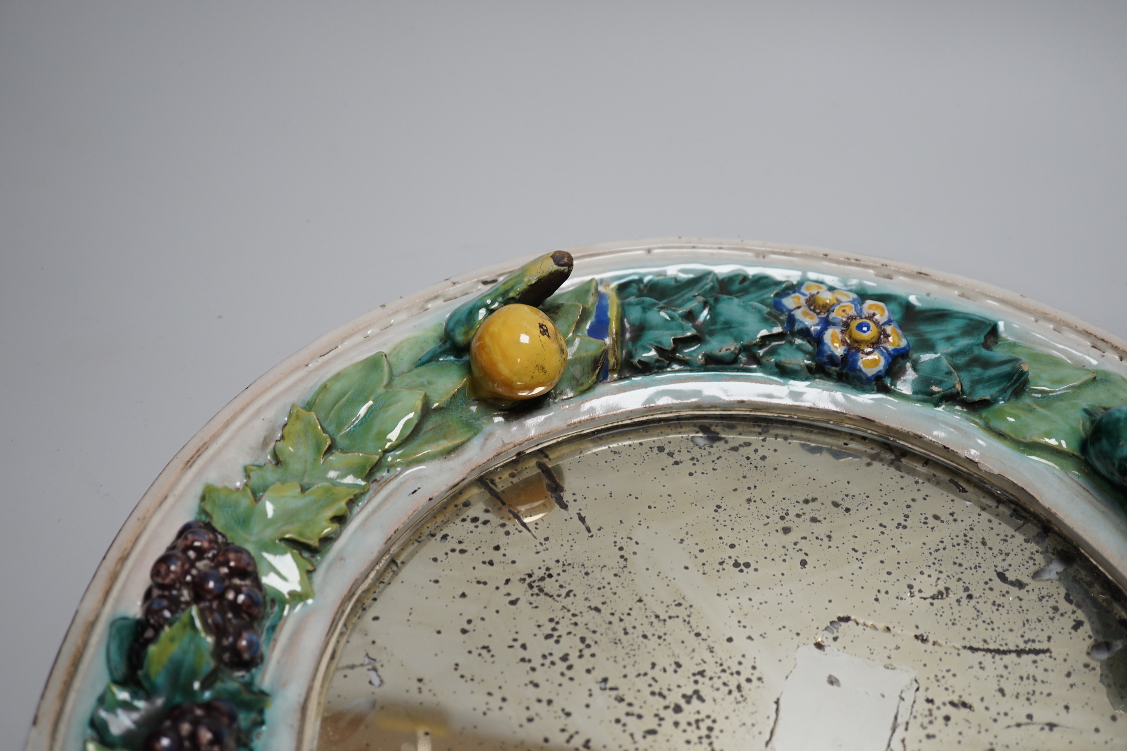 A circular earthenware mirror, possibly by Della Robbia Pottery of Liverpool, decorated with foliage and fruit, 37cm
